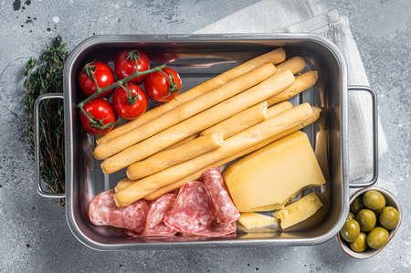 Appetizer platter with grissini bread sticks, salami, tomato and parmesan cheese. Gray bakground....