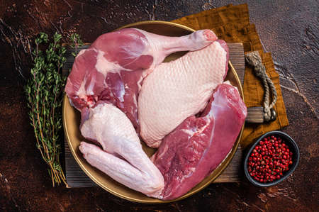 Fresh duck meat parts, raw breast steak, legs, wings in a plate with herbs. Dark background. Top viewの写真素材