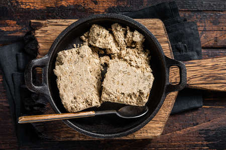 Halva with sunflower seeds and honey in pan. Wooden background. Top view
