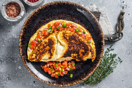 Stuffed egg omelet with tomato, onion and herbs on a plate. Gray background. Top view