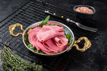 Thin slices of ham in a skillet with arugula salad. Black background. top view.の写真素材
