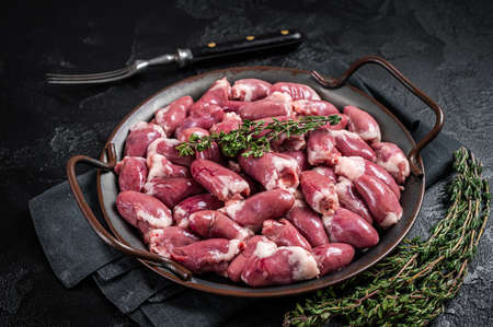 Raw chicken hearts in a steel tray with thyme. Black background. top view.