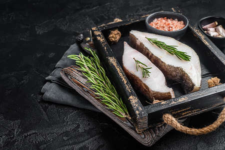 Raw halibut fish steak in wooden tray with herbs. Black background. top view. copyspace.の写真素材