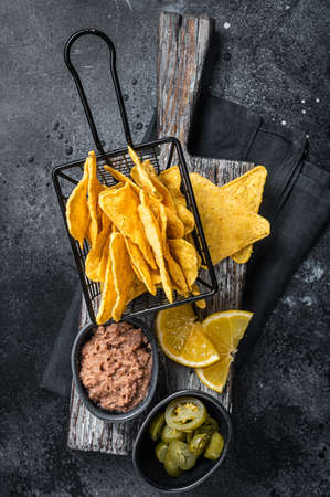 Mexican nachos corn chips with Chili con carne and jalapeno in a basket. Black background. top view.