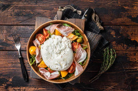 Italian tomatoes and burrata cheese salad with arugula, prosciutto ham and olives. wooden background. top view.の写真素材