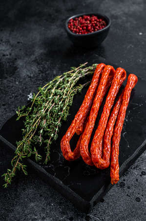 Smoked kabanos sausages with herbs on marble board. Black background. top view.