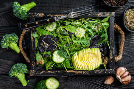 Vegetarian green salad with salad leaves mix, avocado and vegetables. Black wooden background. top...
