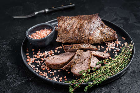 Barbecue dry aged wagyu Tri Tip beef steak on a plate with pink salt. Black background. top view.