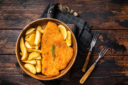 Austrian fried weiner schnitzel with potato wedges in a wooden plate. wooden background. top view.