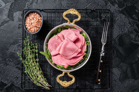 Thin slices of ham in a skillet with arugula salad. Black background. top view.の写真素材