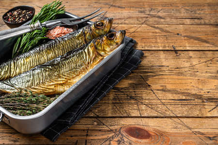 Smoked marinated herring fish in kitchen tray with herbs. wooden background. top view. copyspace.