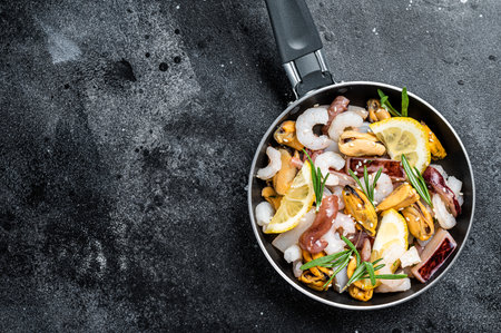 Raw mix seafood cocktail with shrimps, prawns, mussels, squids and octopus in a skillet ready for cooking. Black background. Top view. Copy spaceの写真素材