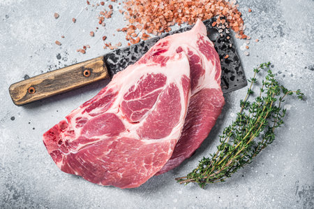 Fresh pork tender steaks from raw neck meat on butcher meat cleaver with salt and thyme. gray background. top view.の写真素材