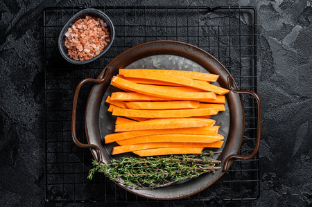 Sliced Sweet potatoes in a steel tray, fresh batata fries ready for cooking. Black background. top view.の写真素材