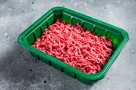 Raw Minced Meat in a Plastic Container, ground beef. gray background. top view.