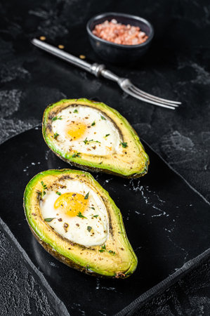Eggs baked in avocado with herbs and spices. Black background. top view.の写真素材