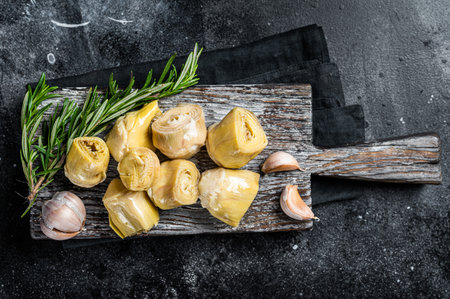 Artichokes hearts marinated with olive oil and herbs, pickled artichoke with garlic on wooden board. Black background. top view.の写真素材