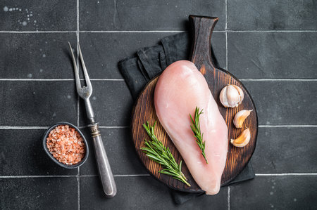 Raw chicken breast fillet on a wooden board with rosemary and garlic, poultry meat. Black background. top view.の写真素材