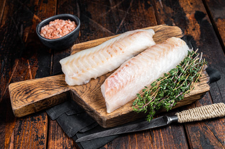 Cod fish fillets, raw codfish with thyme on wooden board. wooden background. top view.