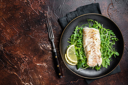 Grilled cod fish fillet served with green salad in a plate. dark background. top view. copyspace.