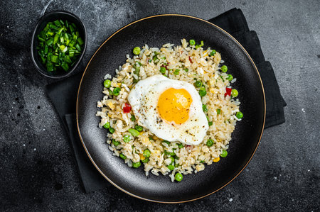 Fried rice with chicken, egg and vegetables in a plate. Black background. top view.の写真素材