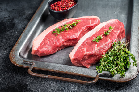 Top sirloin steak, raw beef meat steak with thyme and pepper on steel tray. Black background. top view.の写真素材