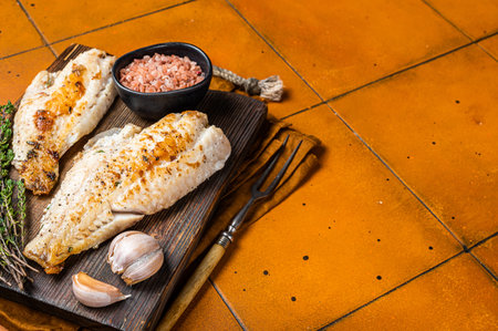 Roast sea red perch fillet, redfish fish on wooden board. Orange background. Top view. Copy space