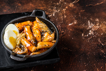 Korean Topokki or Tteokbokki rice cake with egg and mashrooms. dark background. top view. copyspace.