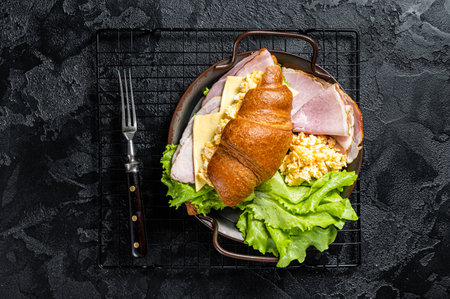 Breakfast croissant sandwich with scrambled eggs, cheese and ham. Black background. top view.の写真素材