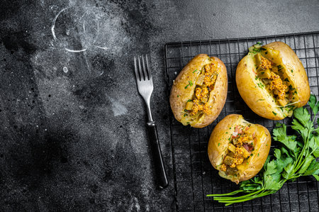 Turkish Kumpir, baked potatoes stuffed with cheese, bacon, salty cucumber, herbs and butter. Black background. top view. copyspace.の写真素材