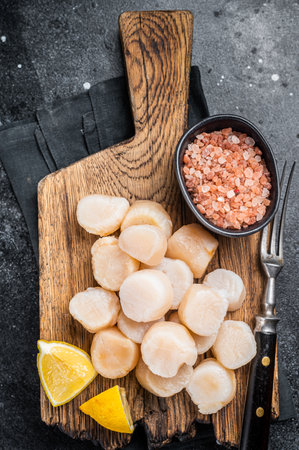 Fresh Raw scallops on a wooden board with sea salt. Black background. Top view.の写真素材