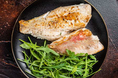 Roasted Snapper, sea red perch fillet on a plate with salad. dark background. top view.