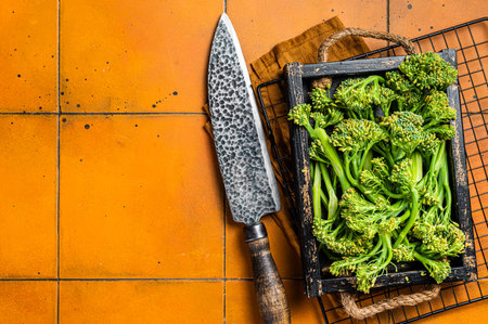 Raw green baby Broccolini in a wooden tray. orange background. top view. copyspace.の写真素材