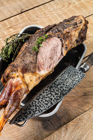 Whole oven roasted goat leg meat with thyme in a steel tray. Wooden background. Top view.の写真素材
