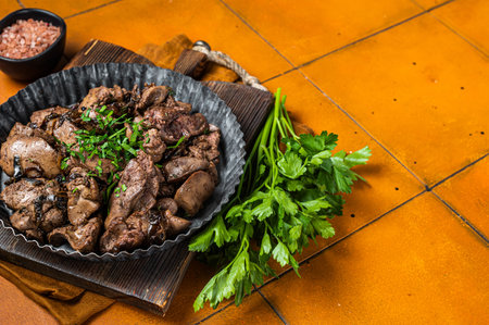 Roast chicken liver with onions and herb in a steel plate. Orange background. Top view. Copy space.の写真素材