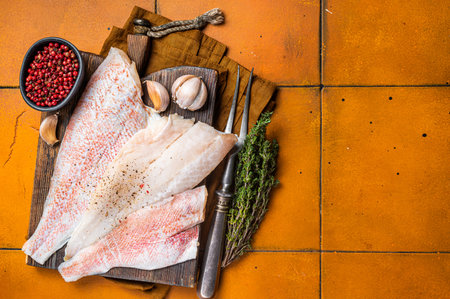 Uncooked ocean red perch fillet, redfish with herbs and spices. Orange background. Top view. Copy spaceの写真素材