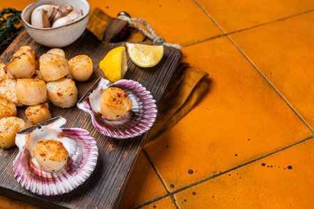 Seared Scallops fillets on a wooden board ready for eat. Orange background. Top view. Copy space.