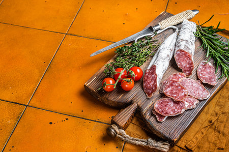 Spanish Fuet sausage slices on wooden cutting board. Orange background. Top view. Copy space.
