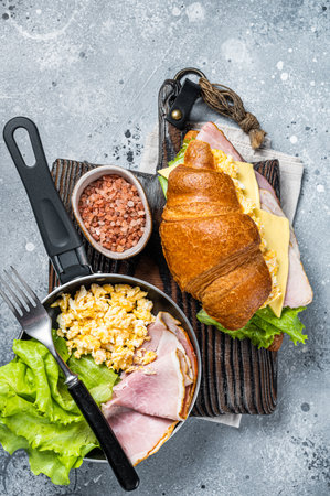 Croissant sandwich with turkey ham, scrambled eggs, cheese and lettuce salad. Gray background. Top view.の写真素材