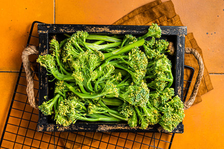 Raw green baby Broccolini in a wooden tray. Orange background. Top view.の写真素材