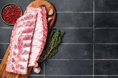 Fresh Pork Spareribs, Raw spare loin ribs on a wooden board with thyme and spices. Black background. Top view. Copy space.の写真素材