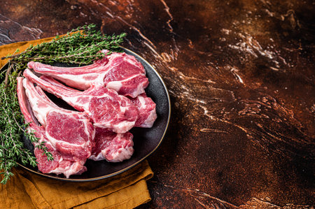Raw lamb chops, fresh mutton meat cutlets on a ribs. Dark background. Top view. Copy space.