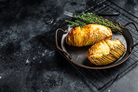 Baked hasselback potatoes with cheese, garlic, thyme and rosemary. Black background. Top view. Copy space.の写真素材