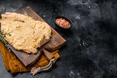Wiener breaded raw pork Schnitzel, meat steak on a wooden board. black background. top view.の写真素材