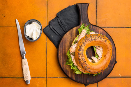 Breakfast Bagel with smoked salmon, lettuce and cream cheese on a wooden board. orange background. top view.の写真素材