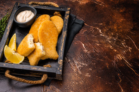 Crusted Fish sticks fingers with lemon and tartar sauce in wooden tray. brown background. top view.の写真素材