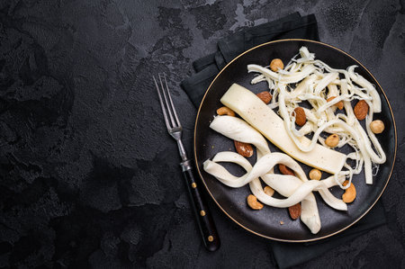 Smoked Traditional Chechil white cheese on a plate with nuts, black background
