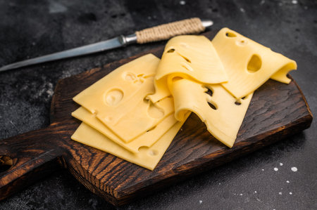 Swiss emmental cheese slices on wooden cutting board. black background. top view.