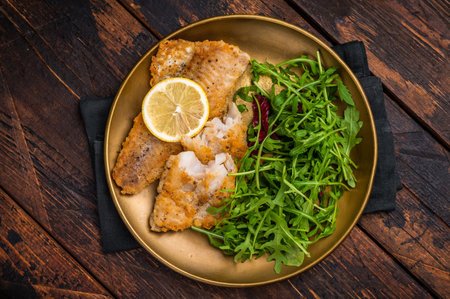 Roasted Pollock fish fillet on a plate with salad. wooden background. top view.