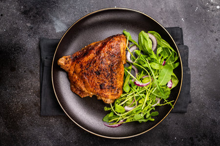 Roasted chicken thigh with salad on a plate, poultry meat. black background. top view.の写真素材